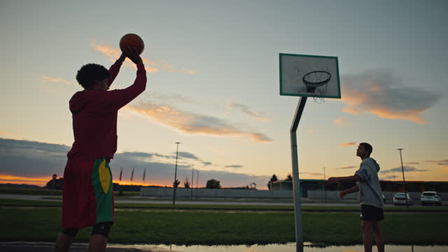 Slow motion shot of a young basketball player passes balls to a teammate who practicing free throws into the hoop.